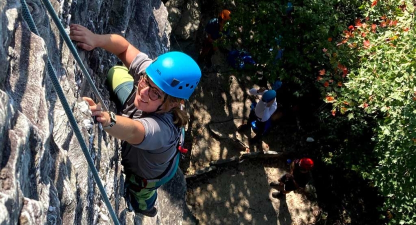 From above, you can see a rock climber wearing safety gear making their way up a rock wall